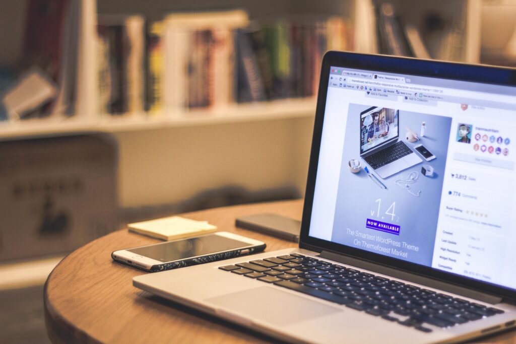 A cozy modern workspace featuring a laptop displaying a website, a smartphone, and books on shelves.